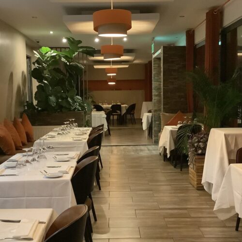 Intérieur moderne d'un restaurant avec un espace de restauration spacieux, tables élégamment dressées, sièges variés et éclairage chaleureux.